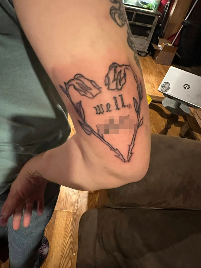 Tattoo on an arm that reads "Well Sh*t" within a heart of thorny roses.