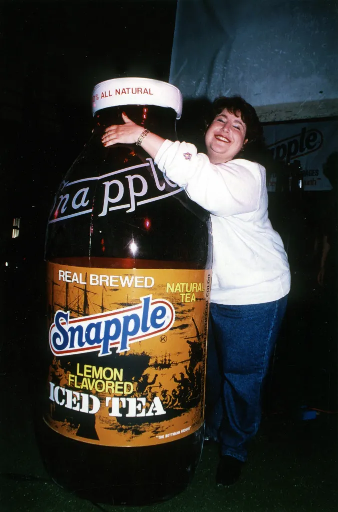 Wendy Kaufman, the Snapple Lady, hugs an oversized Snapple Lemon Flavored Iced Tea bottle.