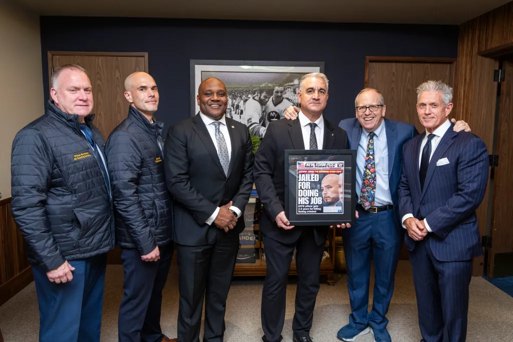 Six men gather, one holding a framed newspaper front page with the headline "Jailed for doing his job."