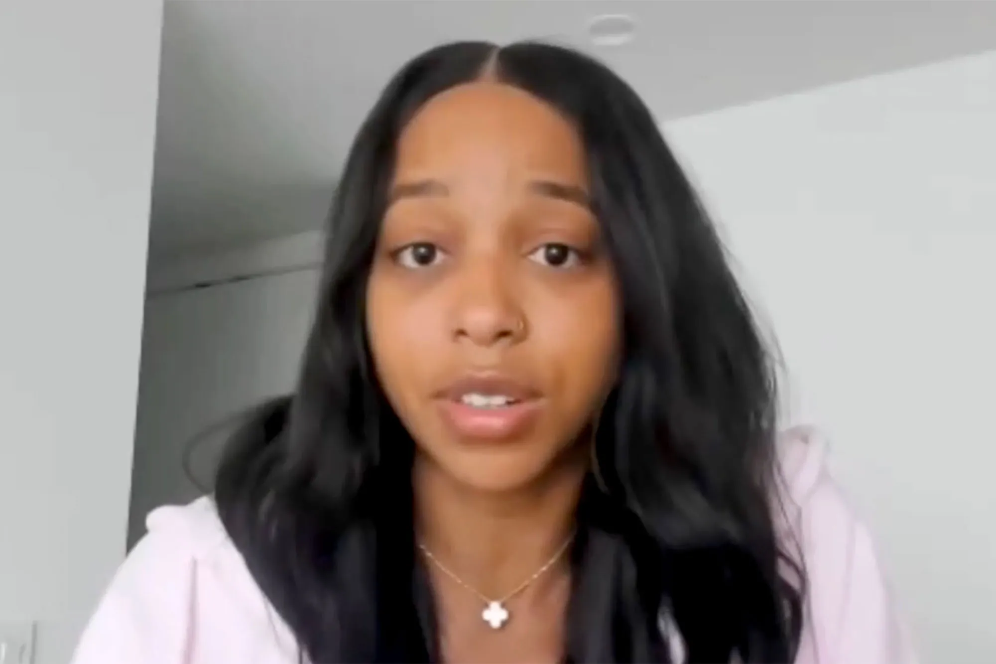 WNBA player Lexie Brown, a Black woman with long dark hair, wearing a light pink hooded sweatshirt and a white clover necklace, speaks to the camera.