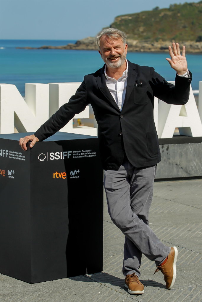 Sam Neill smiling and waving at the 67th San Sebastian Film Festival.