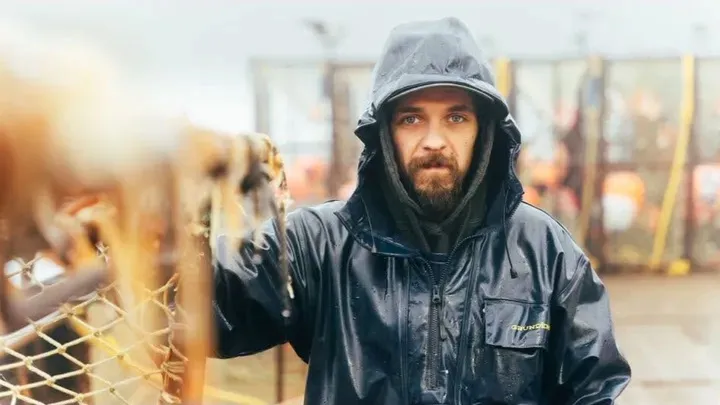 Todd Meadows from Deadliest Catch, dressed in a black waterproof jacket with the hood up, looks directly at the camera.