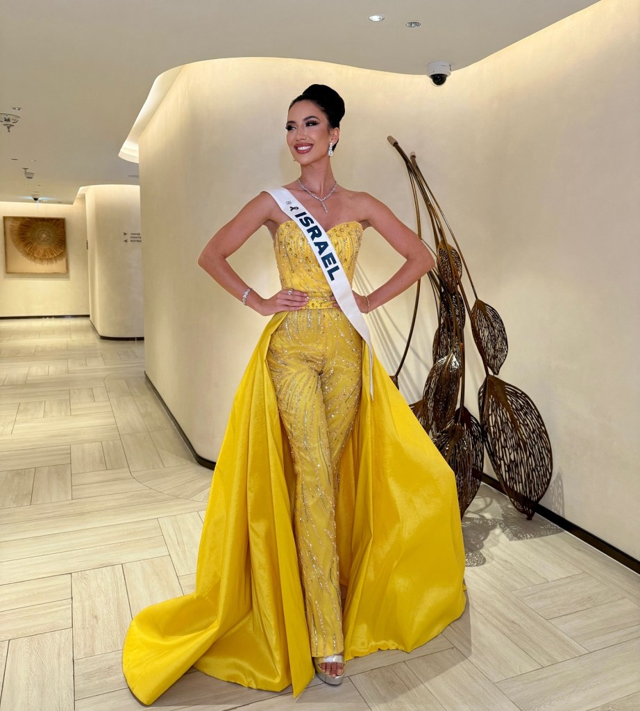 Melanie Shiraz Asor in a yellow jeweled jumpsuit with a long yellow train and "Israel" sash.