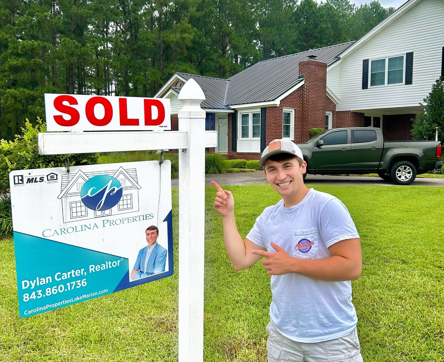 Dylan Carter, a realtor, stands next to a "SOLD" sign in front of a house.