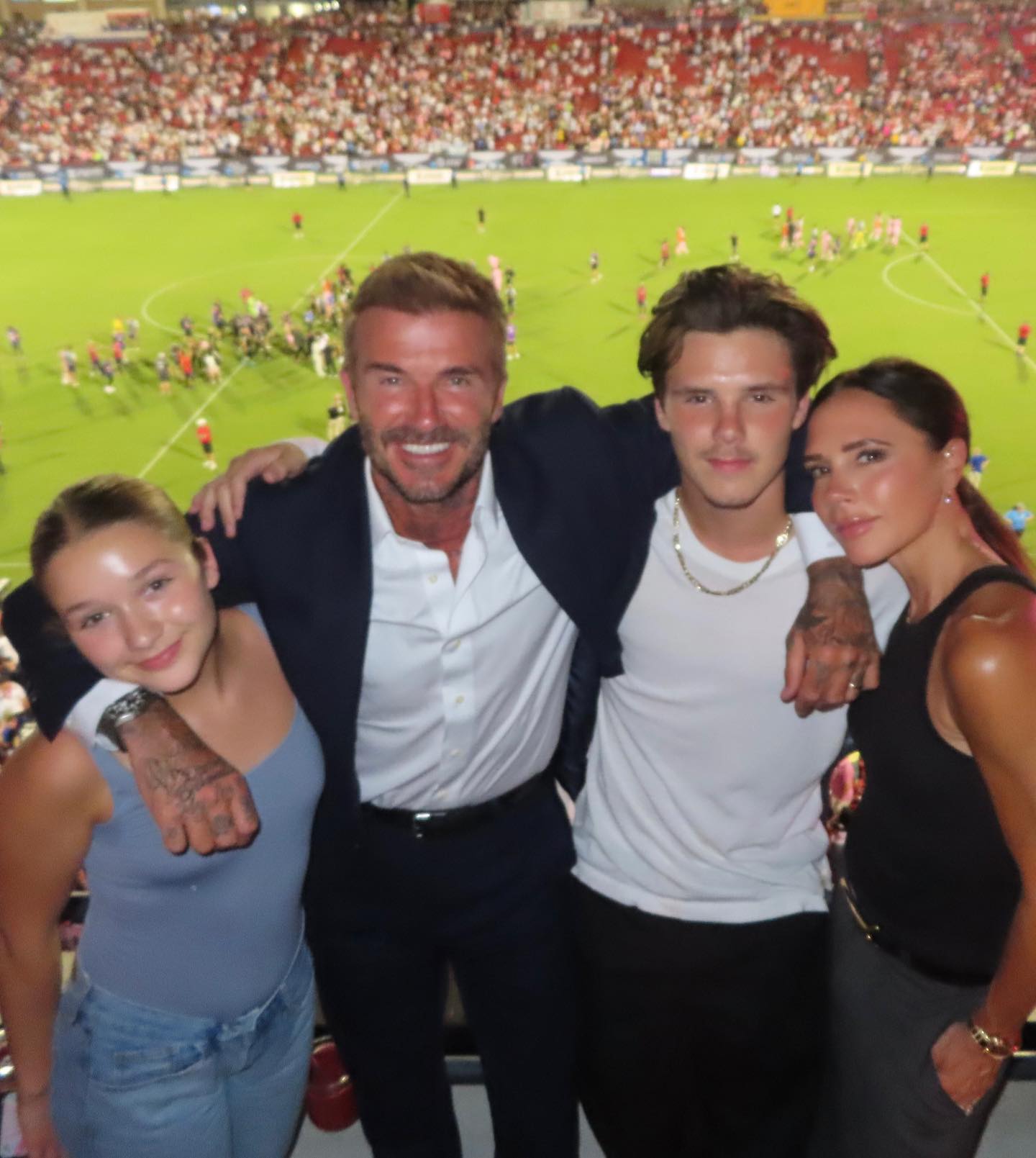 Harper, David, Cruz, and Victoria Beckham pose for a photo with a stadium and field in the background.