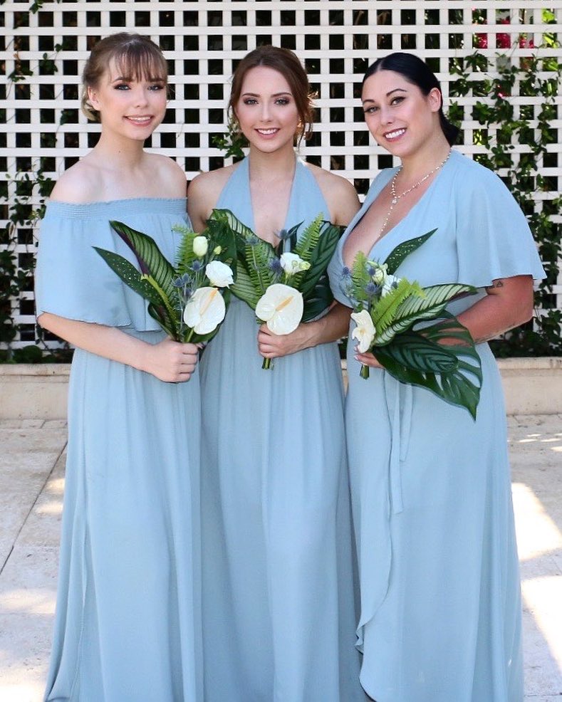 Three women in matching blue dresses and holding bouquets.
