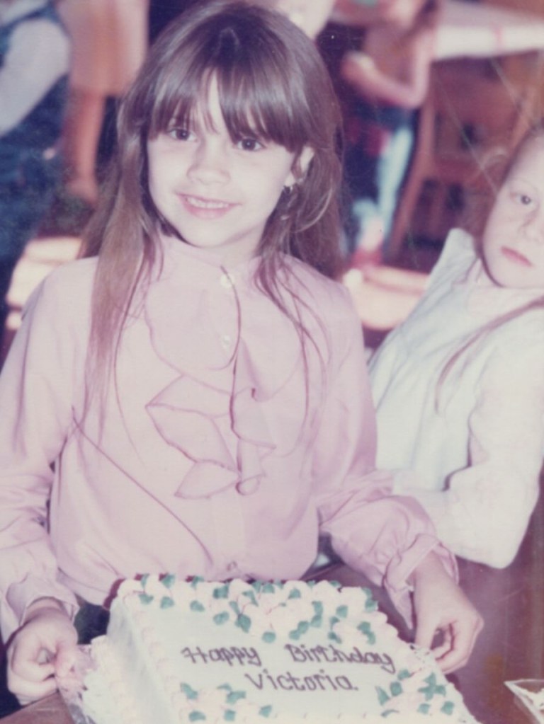 A young Victoria Beckham smiles over a "Happy Birthday Victoria" cake.