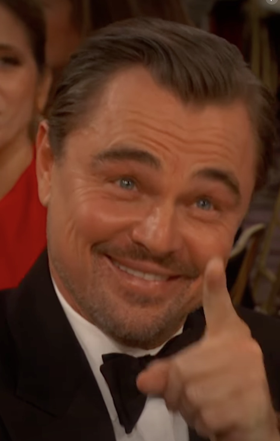 Leonardo DiCaprio smiling and pointing while wearing a tuxedo at the Golden Globes.