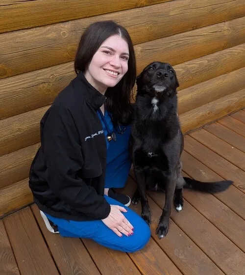Dr. Lynnea Soposki, a veterinarian, kneeling with a black dog.