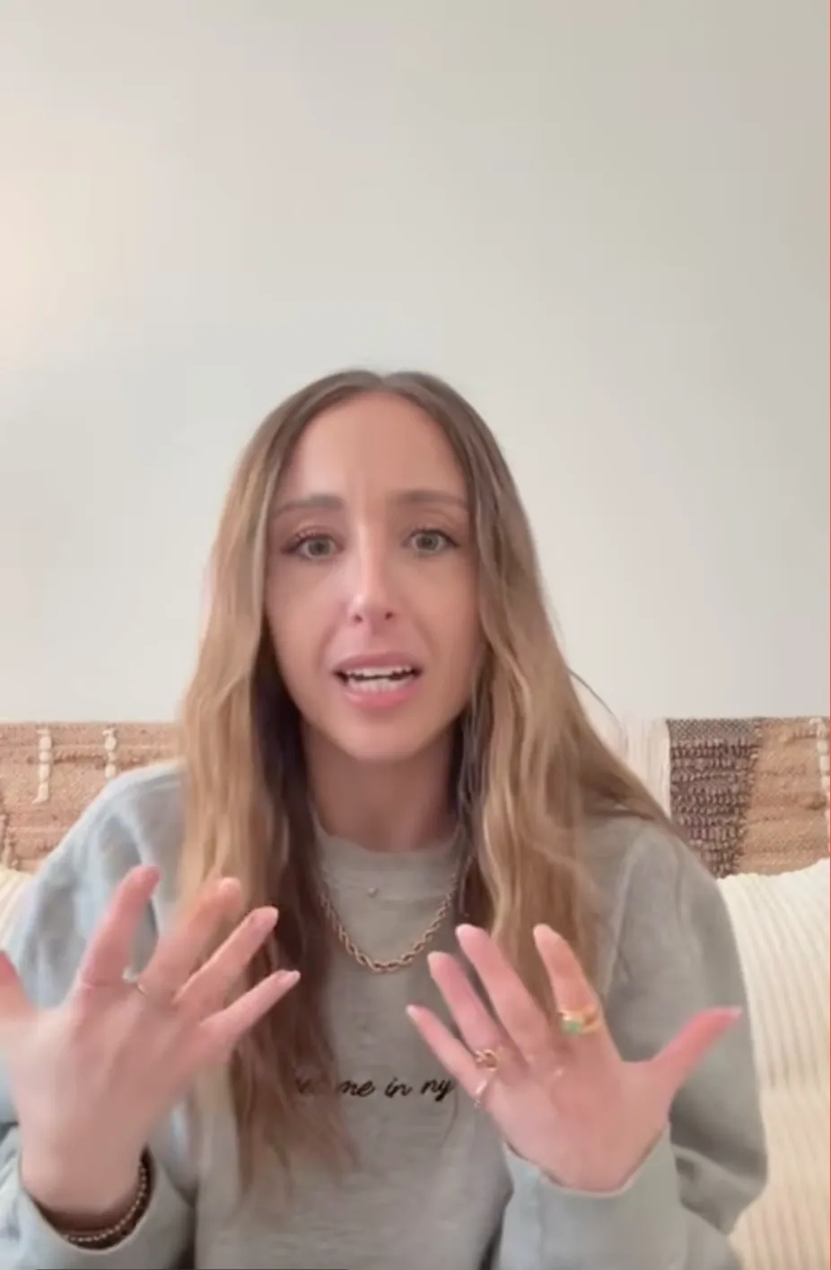A young woman with long, light brown hair speaking and gesturing with her hands.