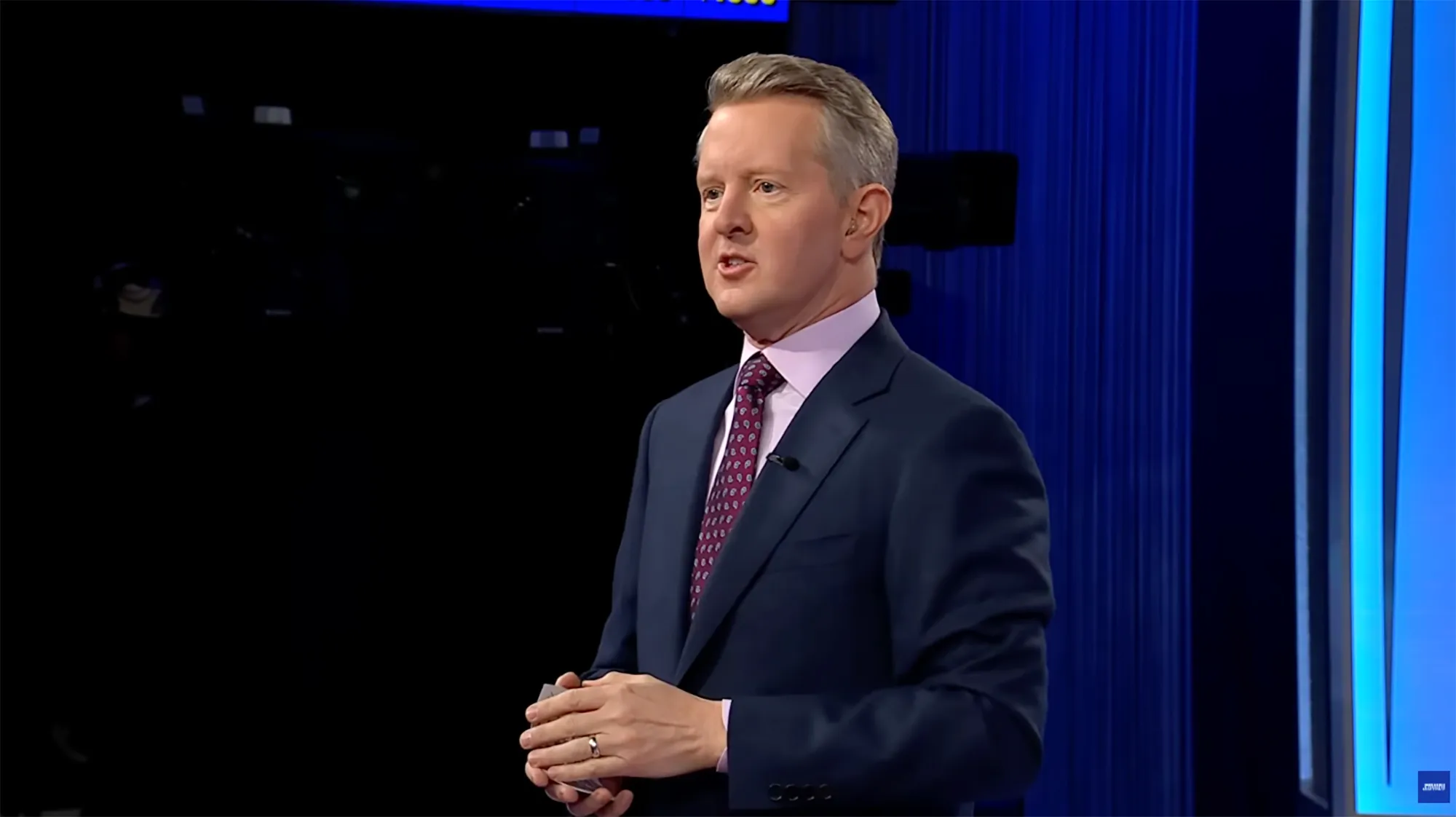 Ken Jennings, host of Jeopardy!, stands holding cards.