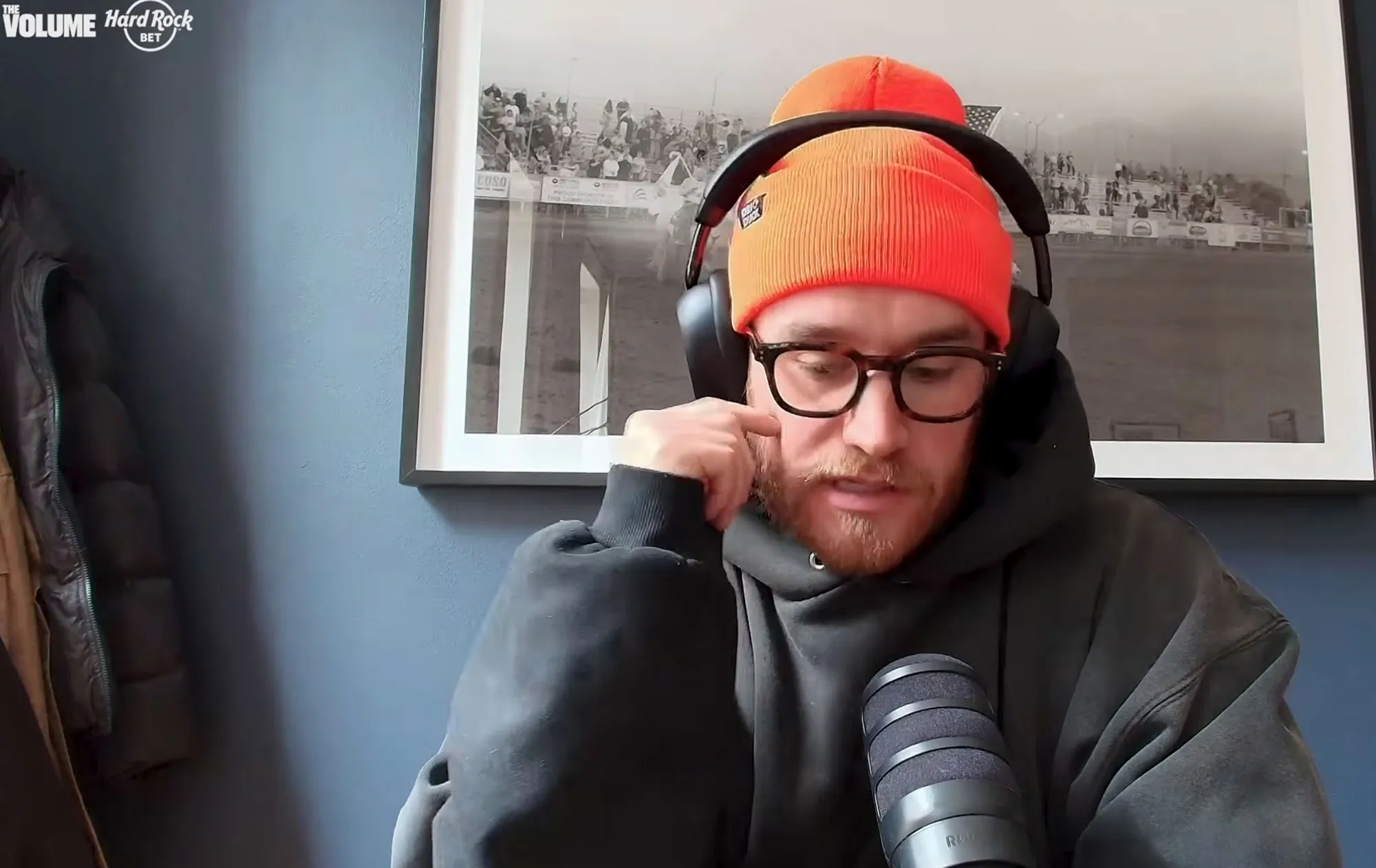 A man in an orange beanie and glasses speaks into a microphone.