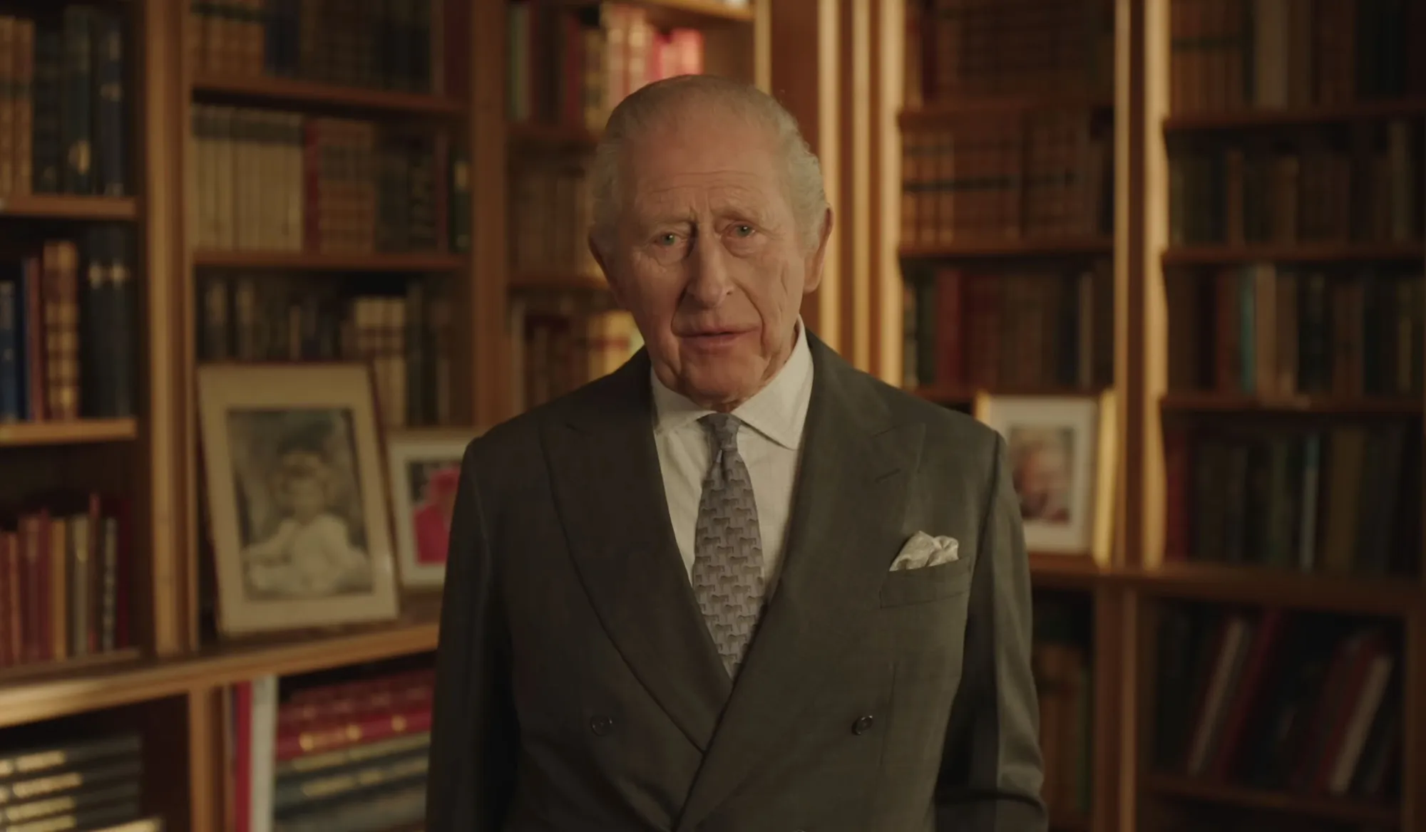 King Charles III speaking to the camera in front of a bookshelf.