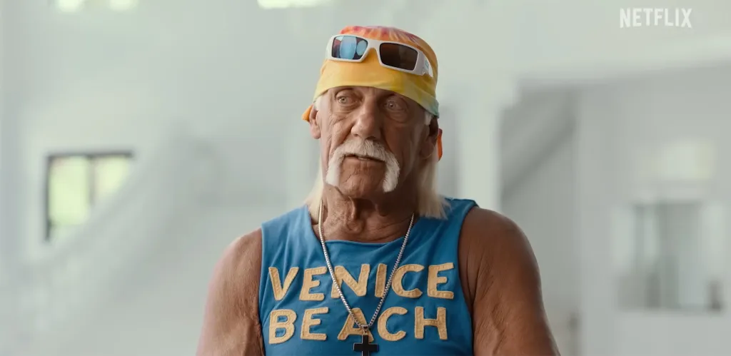 Hulk Hogan wearing a colorful headband with sunglasses, a blue "Venice Beach" tank top, and a silver chain with a cross.