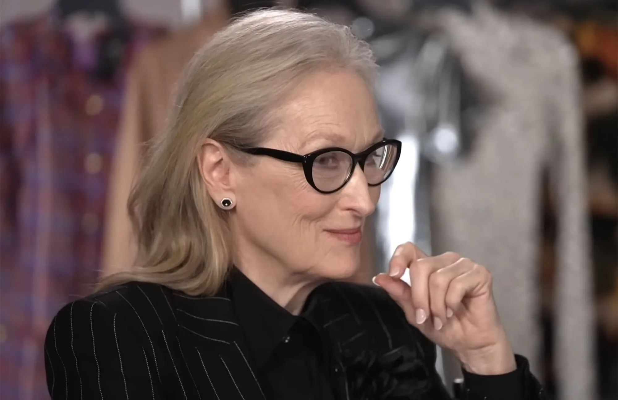 Meryl Streep wearing glasses, a black pinstripe jacket, and a black shirt.