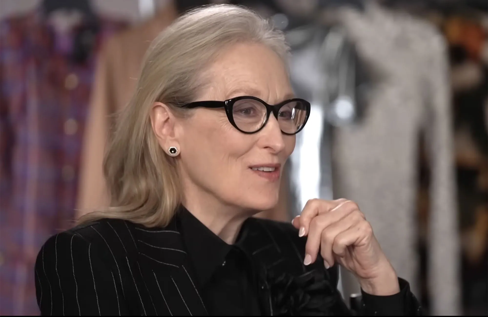 Meryl Streep wearing glasses, a black pinstriped jacket, and a black shirt.