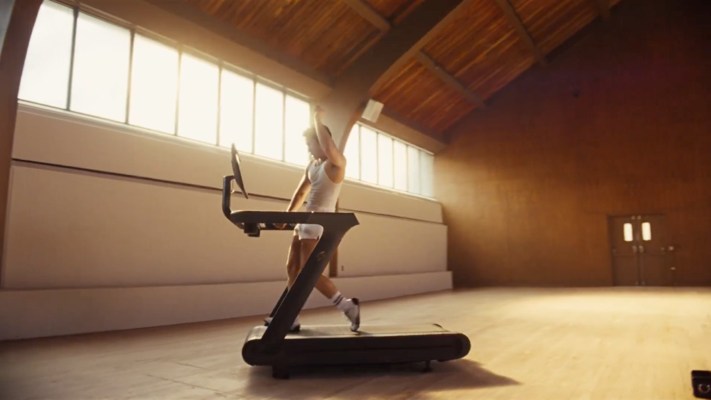 A person in a white tank top and shorts runs on a treadmill.