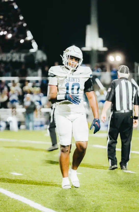Ryder Barnes, wearing a white football uniform with "SAINTS" and the number 10, standing on a football field at night.