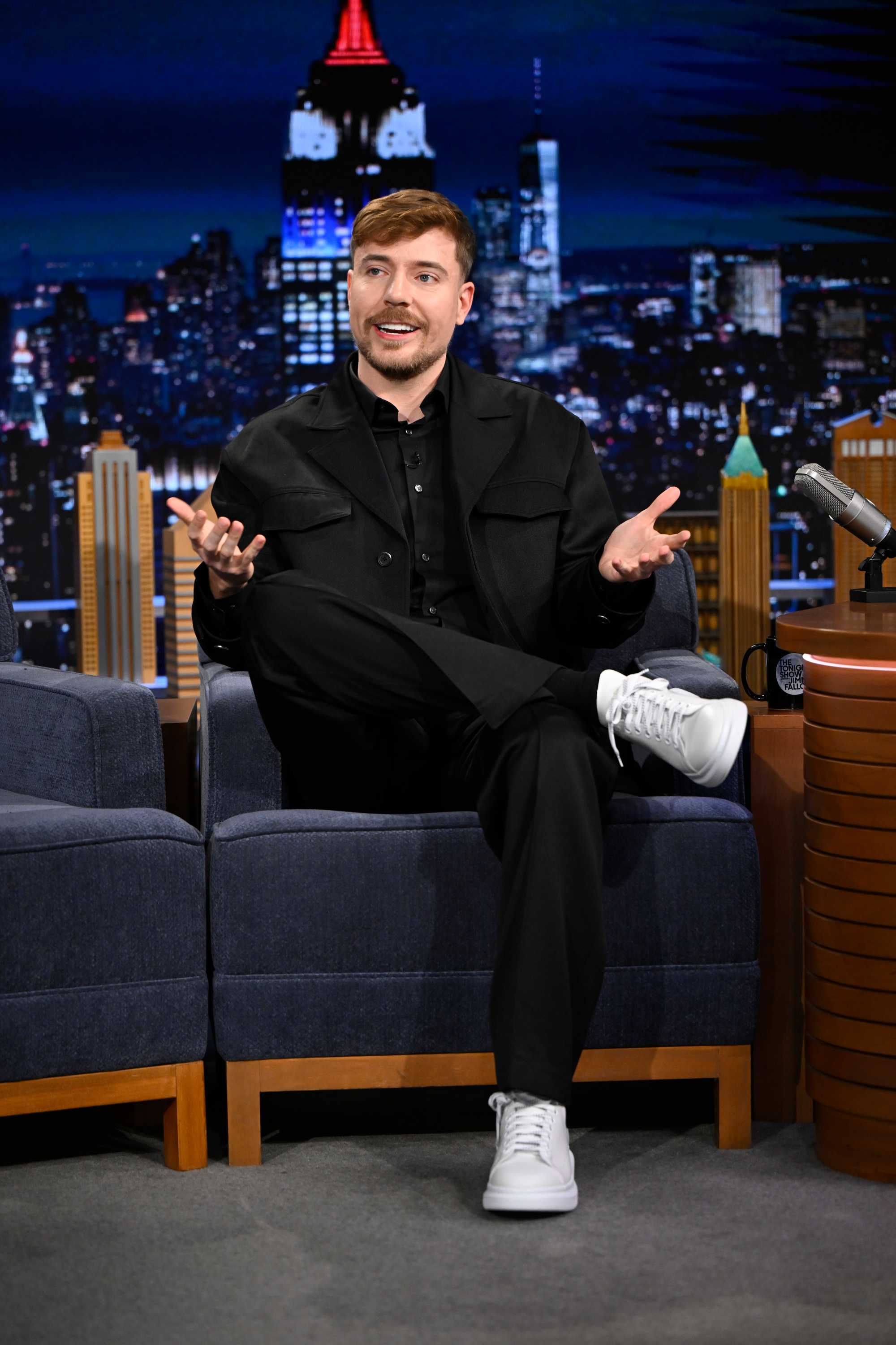MrBeast sits on a talk show set with a cityscape backdrop.
