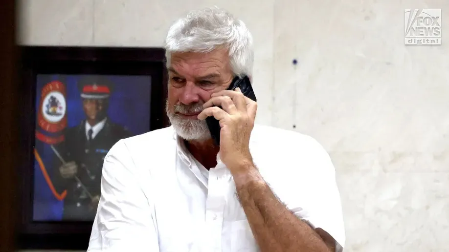 A white-haired man with a beard on the phone.