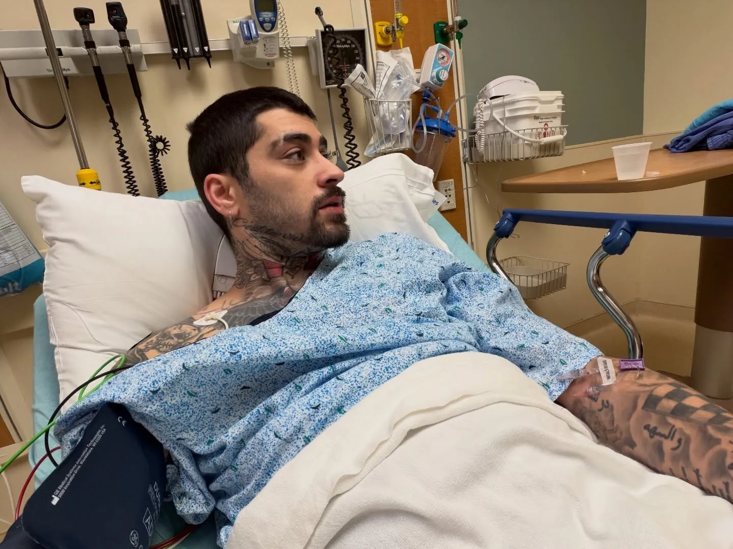 Zayn Malik in a hospital bed with an IV drip and a blood pressure cuff.