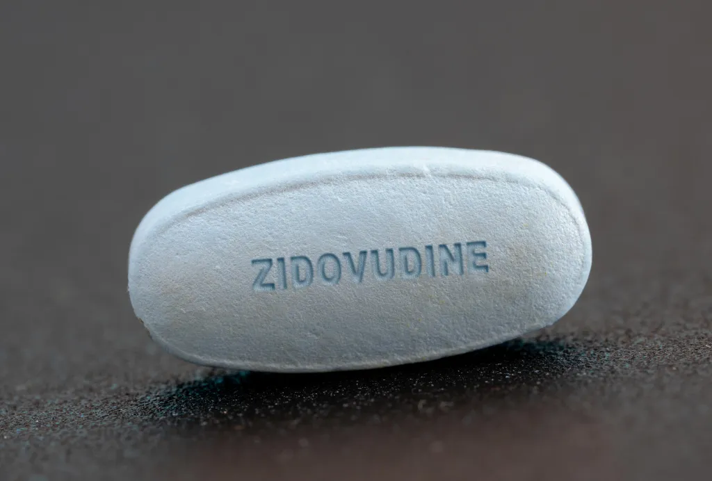 Close-up of a blue pill with "ZIDOVUDINE" embossed on its surface.