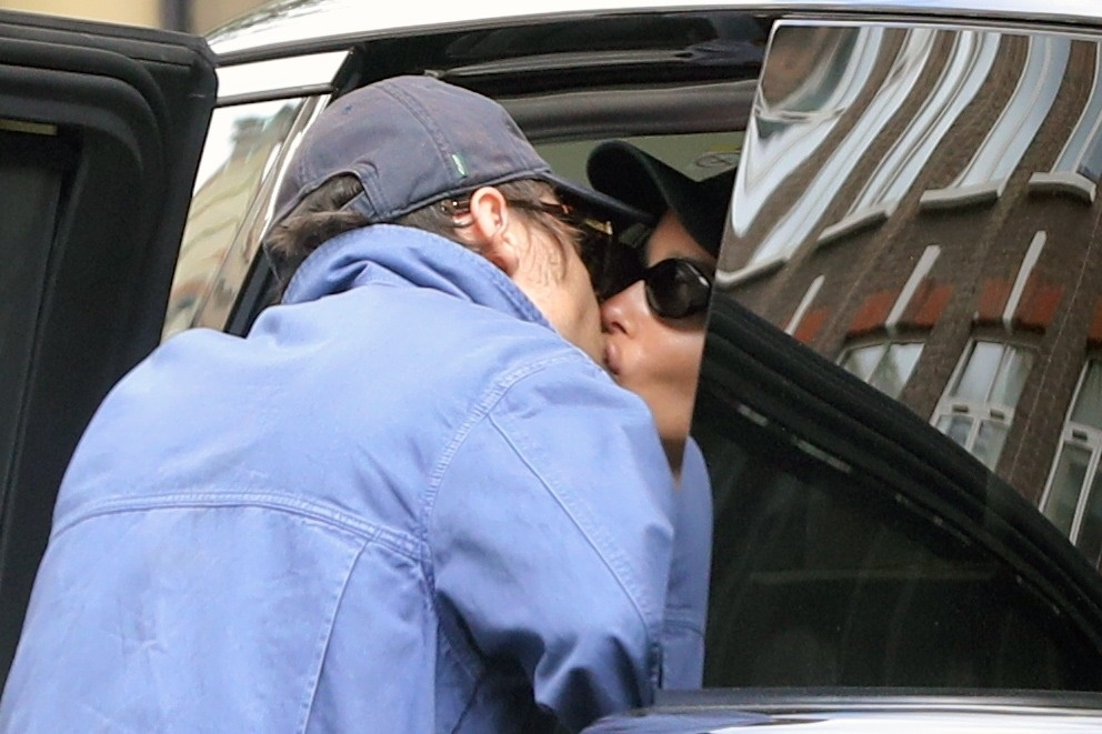 Harry Styles in a blue jacket kissing Zoe Kravitz in sunglasses through a car window.