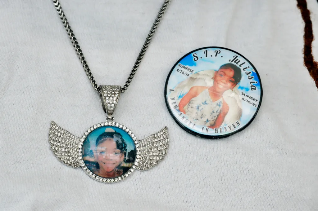 A necklace with a winged pendant showing a photo of Julissia Batties and a button with the text "S.I.P. Julissia A New Angel in Heaven Sunrise 4/26/14 Sunset 8/10/21".
