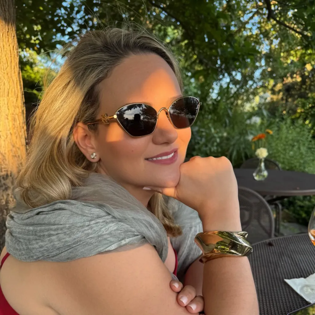 A woman in sunglasses and a gray scarf rests her chin on her hand.