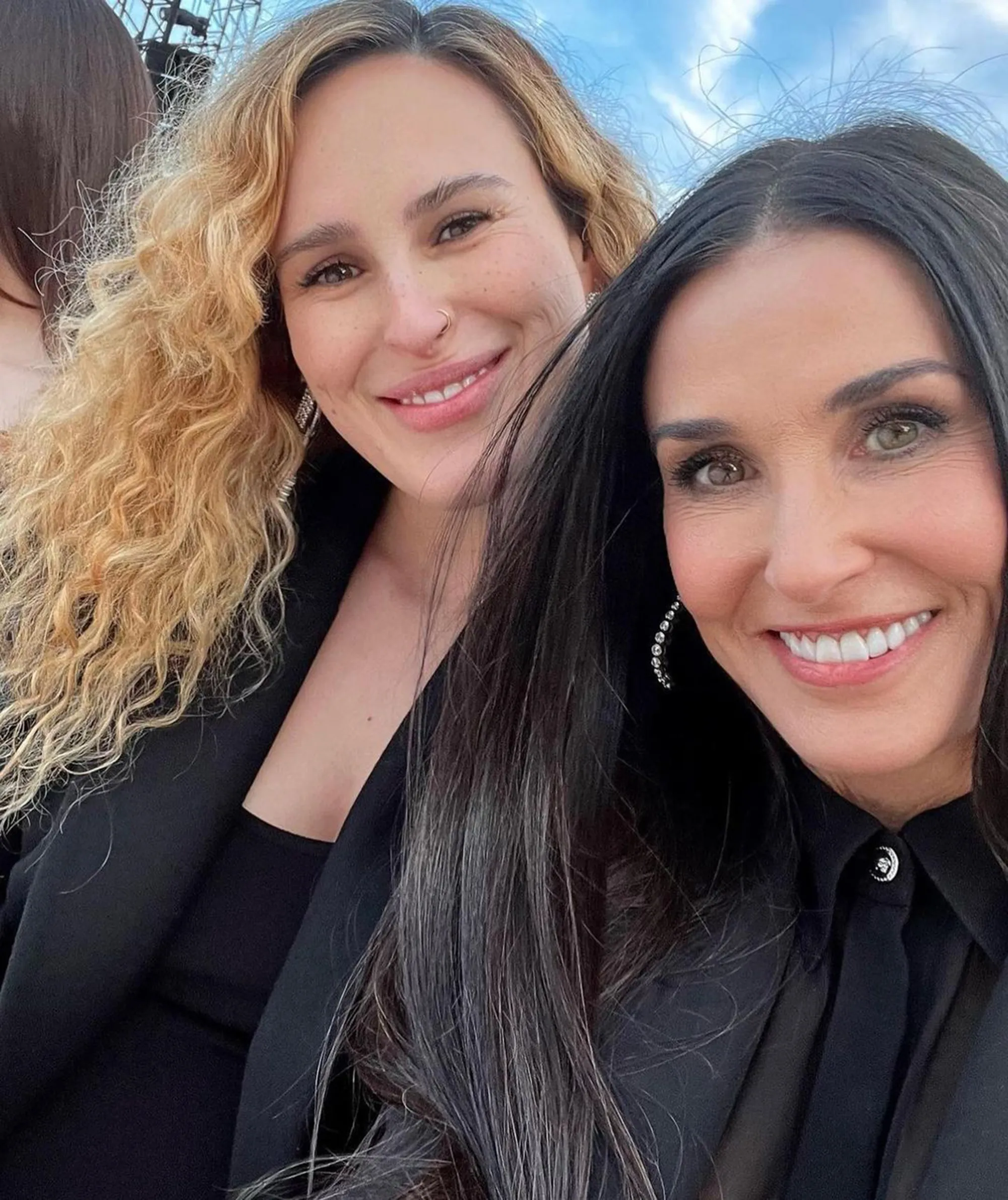 A close-up of a woman with curly blonde hair smiling, next to Demi Moore.