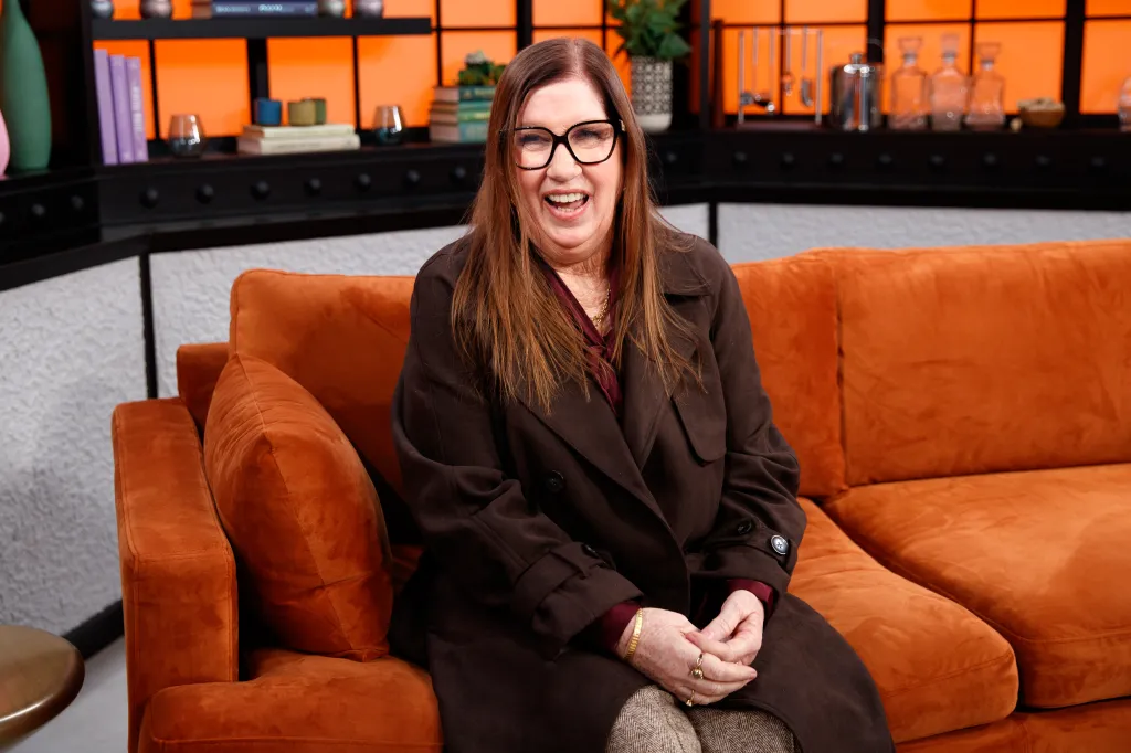 Jenny Slatten laughing while seated on an orange couch.