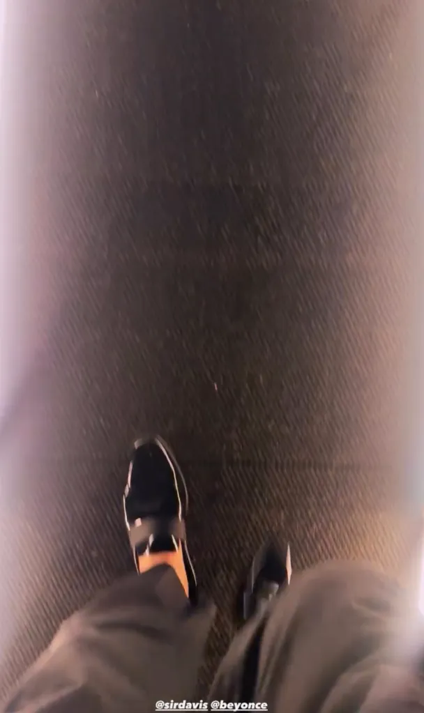 A person's feet in black shoes on a dark textured surface with text 