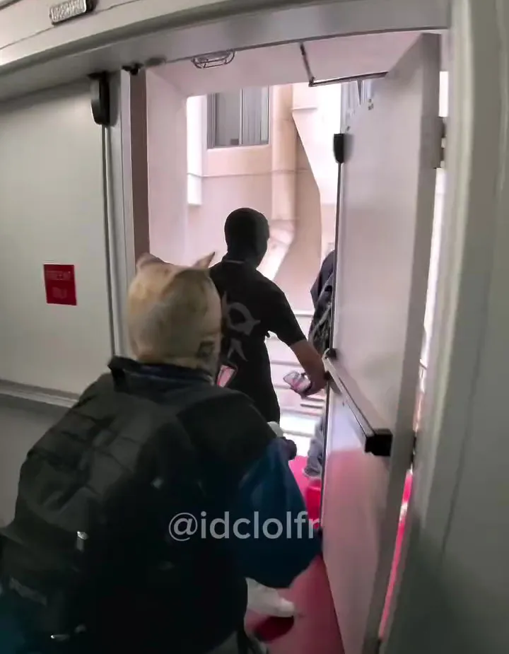People walking through a doorway, one wearing a balaclava.