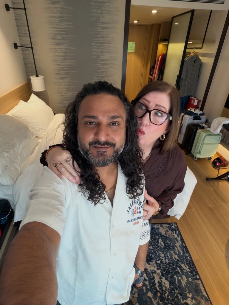 Man with long curly hair taking a selfie with a woman making a kissing face.