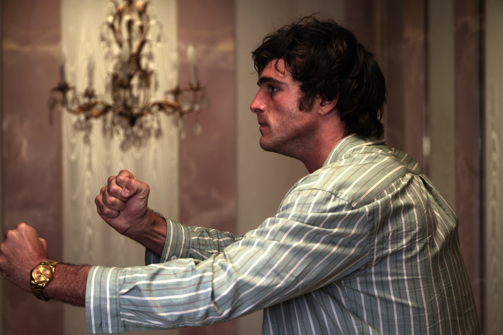 A man with dark hair in a striped shirt makes fists with both hands.