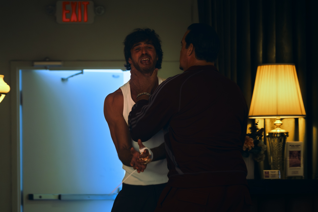 A man in a white tank top is being choked by another man in a dark tracksuit.
