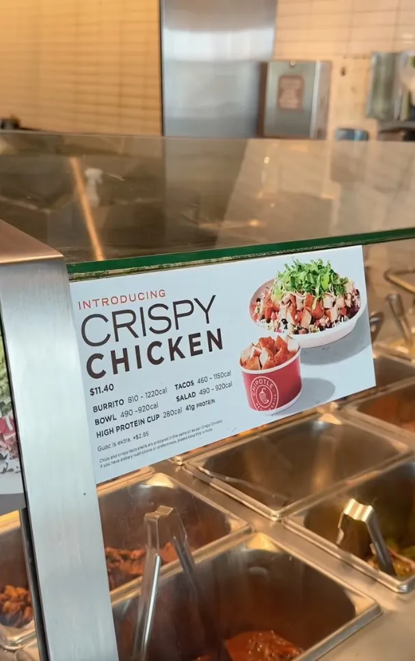 A sign at a Chipotle Mexican Grill introducing "Crispy Chicken" with pricing and calorie information.