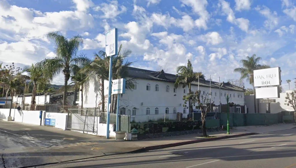 Exterior view of the Oak Tree Inn, a white building with several palm trees, and signs for "Quik Wash" and "Oak Tree Inn".