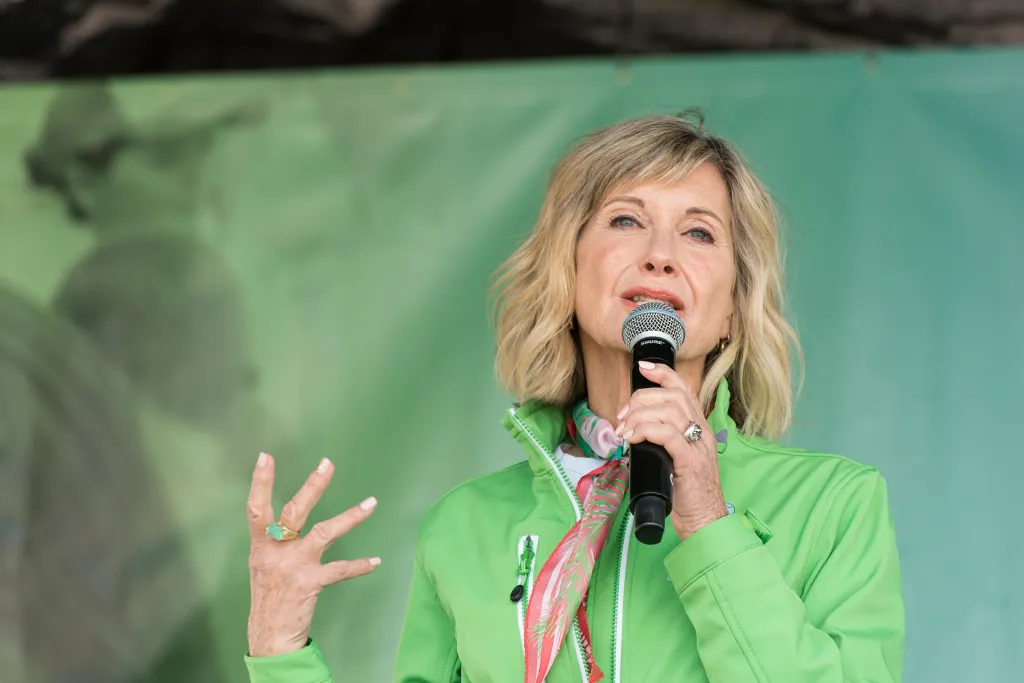 Olivia Newton-John speaking into a microphone at the annual Wellness Walk and Research Run.
