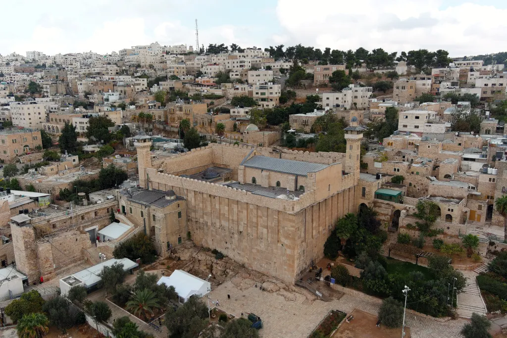Aerial view of the Cave of the Patriarchs, with a minaret on the left and a dense city of homes on a hill in the background.