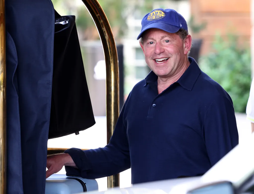 CEO of Activision Blizzard, Bobby Kotick, smiles, wearing a blue polo shirt and a blue cap with a yellow "RAMS FOOTBALL" logo.