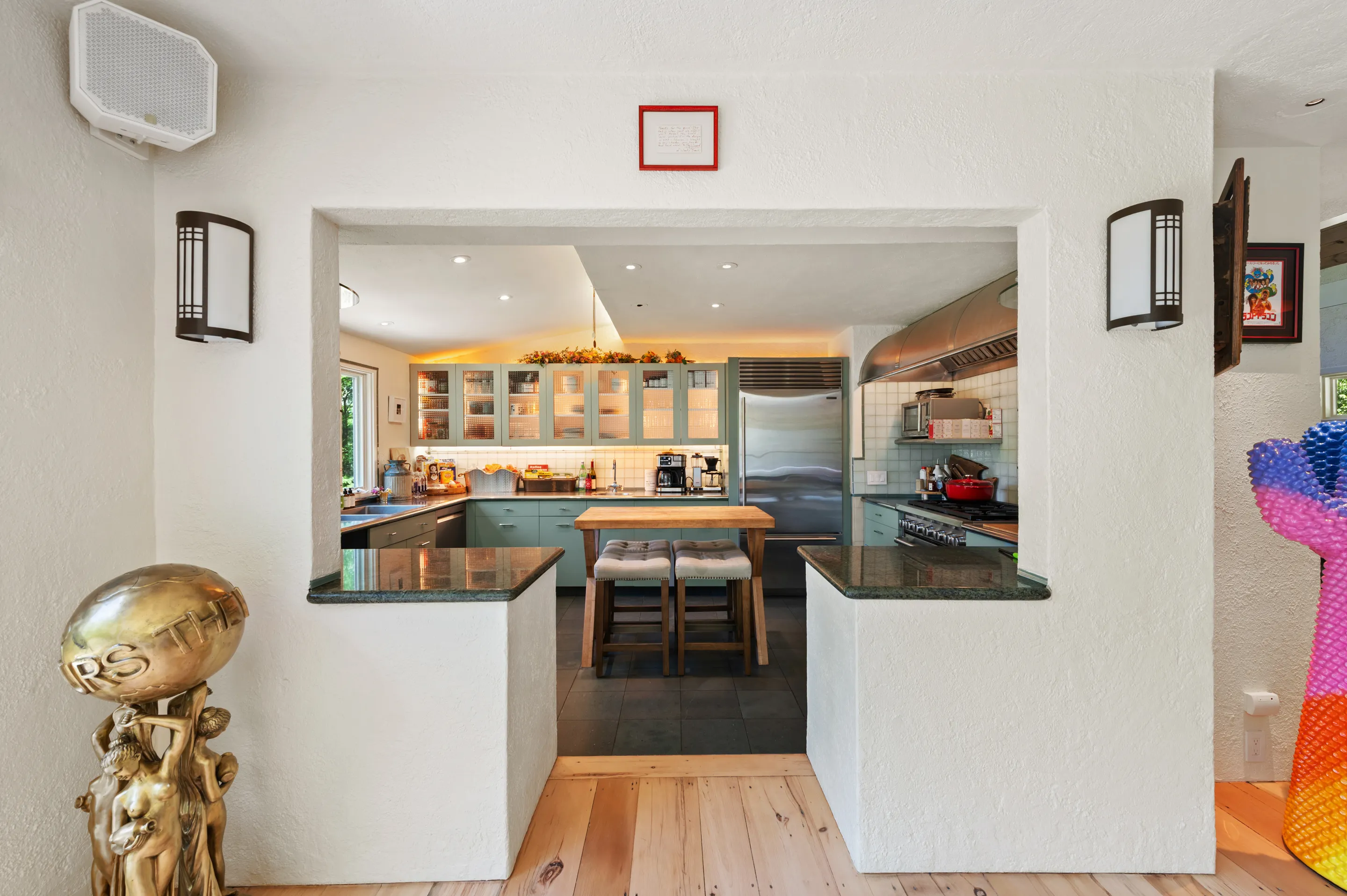 A kitchen with light green cabinets, a kitchen island with two stools, and a large refrigerator.