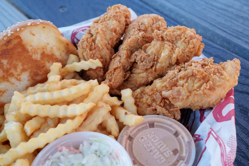 Raising Cane's fried chicken tenders, crinkle-cut fries, coleslaw, and Cane's Sauce in a basket.