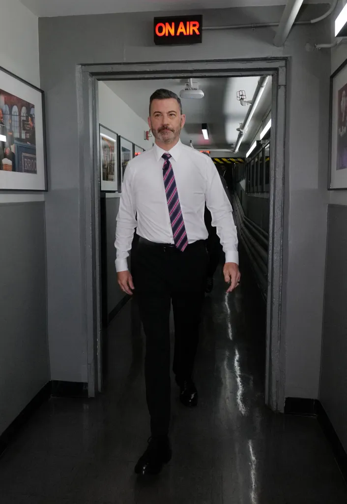 Jimmy Kimmel walks towards the camera in a hallway with an "ON AIR" sign above him.