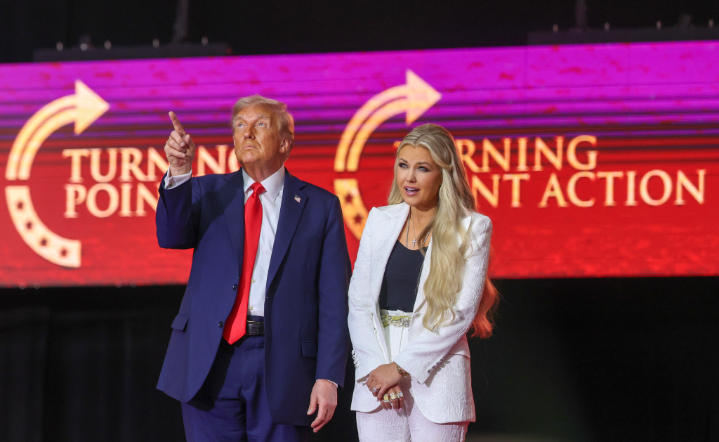 Donald Trump and Erika Kirk onstage at a memorial service, with a "Turning Point Action" banner in the background.