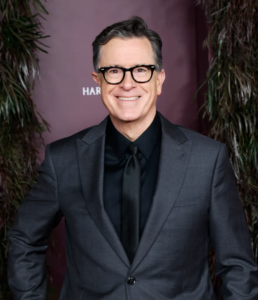 Stephen Colbert posing in a dark gray suit with a black shirt and tie at the WSJ. Magazine 2025 Innovator Awards.