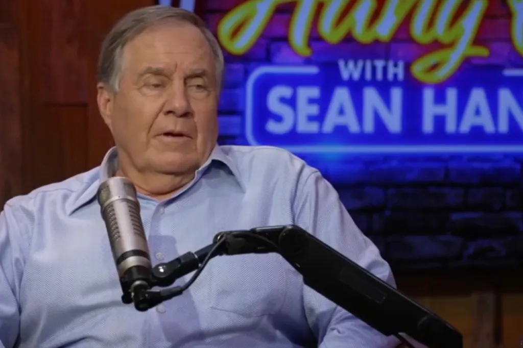 Bill Belichick speaking into a microphone with a neon "Hang Out with Sean Hannity" sign in the background.