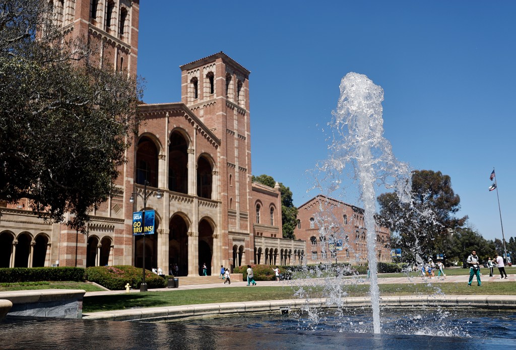 A fountain sprays water into the air in front of Royce Hall at UCLA, with people walking on the plaza.