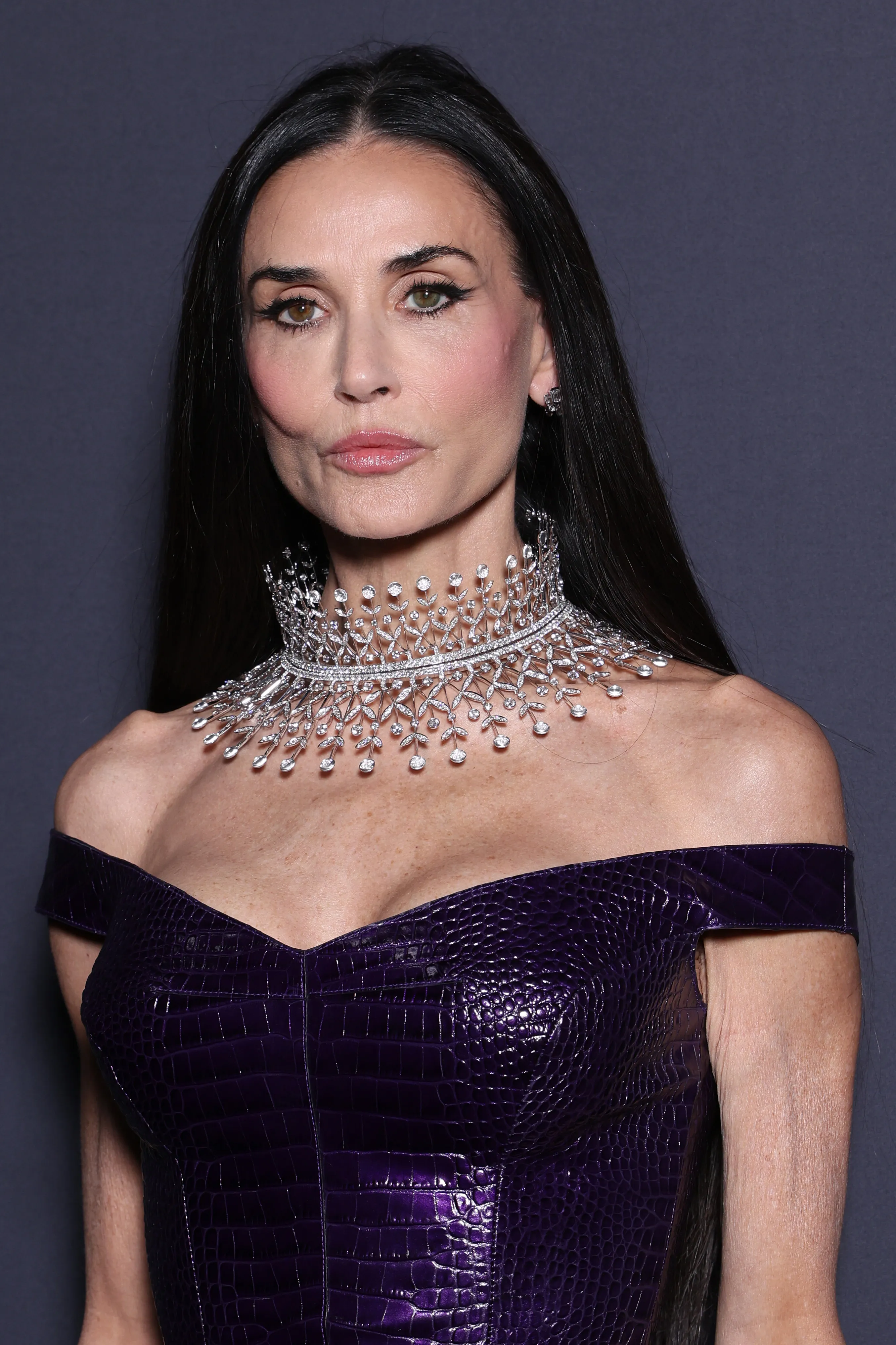 Demi Moore wearing a purple dress and an elaborate diamond necklace.