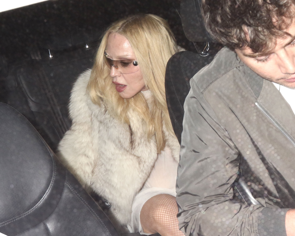 Madonna wearing a white fur coat and sunglasses in the back of a car with David Banda.